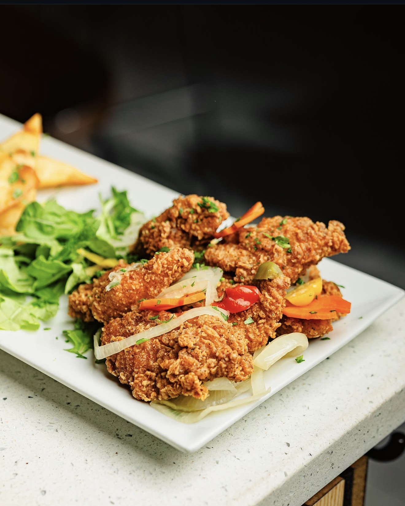 Plate of crispy fried chicken with pickled peppers, onions and greens
