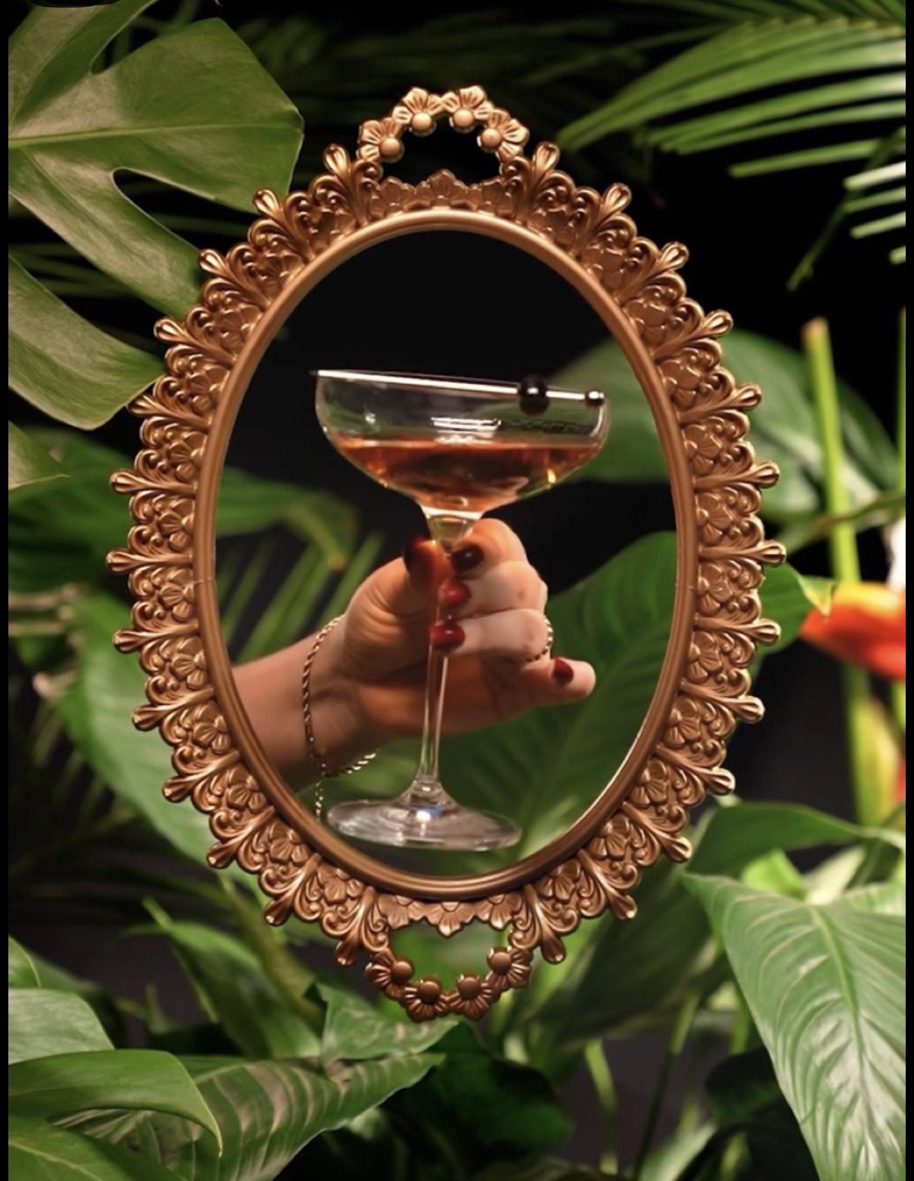Ornate gold-framed mirror reflecting a cocktail among tropical leaves