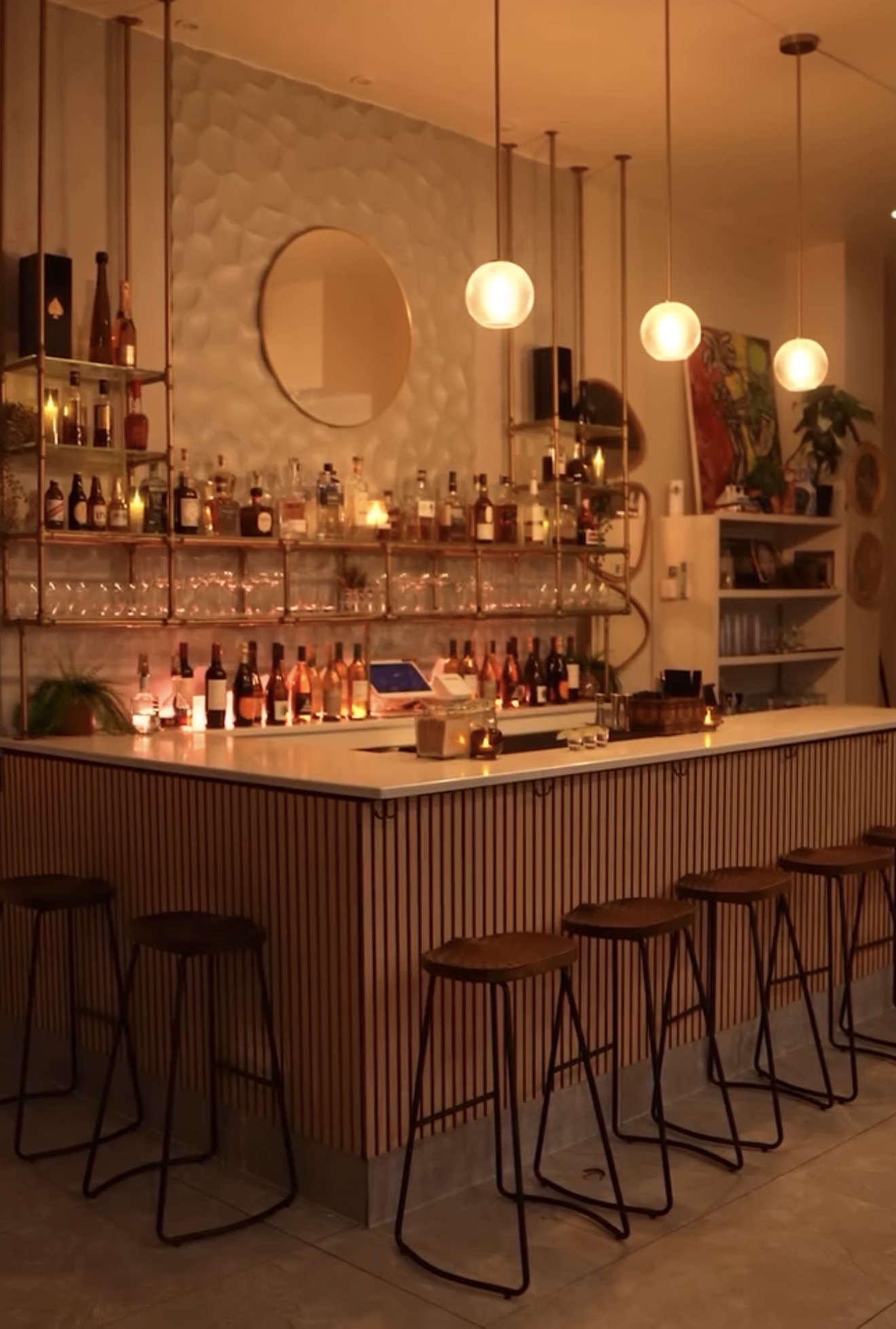Warmly lit cocktail bar with pendant globe lights and brass shelving