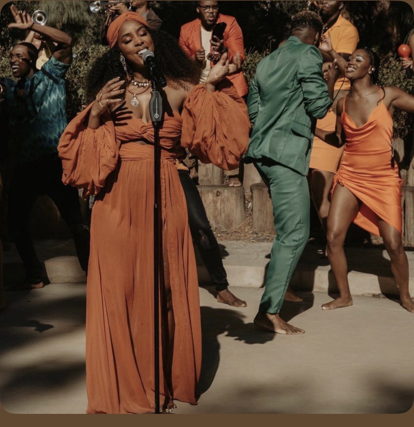 Singer performing outdoors with dancers in orange and green